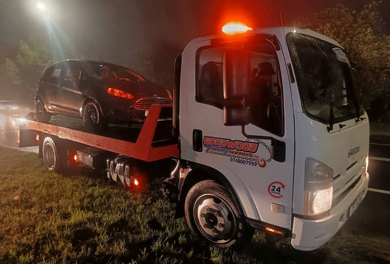Goodwood Towing Services flatbed truck carrying a car at night