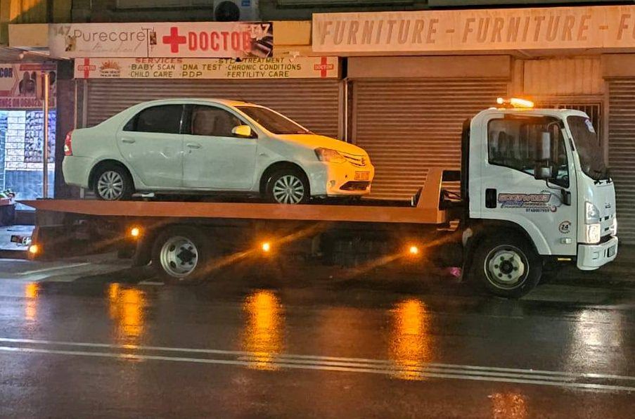 Flatbed carrying a sedan on a wet street at night